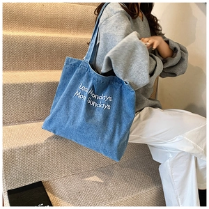 Detail of light blue denim tote bag with white embroidery 'Less Mondays More Sundays'