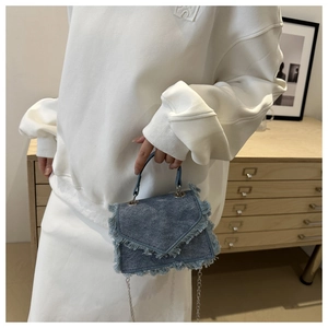Detail der blauen Denim-Tasche mit Fransen und Silberkette vor häuslichem Hintergrund