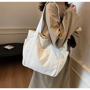 Detail of cream corduroy tote bag featuring canvas straps and front metal buckle pocket