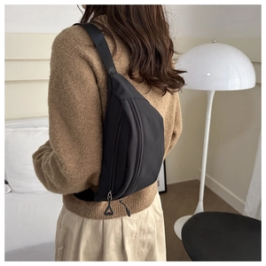 Detail of black ripstop nylon chest bag with dual zippers worn on a model's back