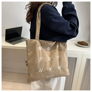 Détail du sac cabas en velours côtelé camel avec broderie porté à l'épaule par un mannequin