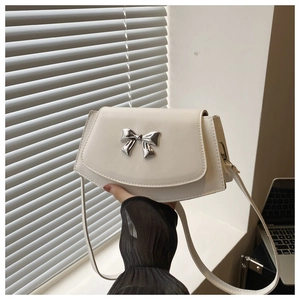 Detail of cream flap crossbody bag featuring a silver metal bow accent and slim strap
