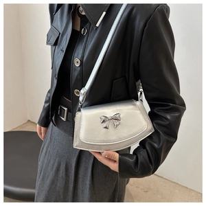 Detail of silver metallic handbag featuring a stylish metal bow and thin strap on a model
