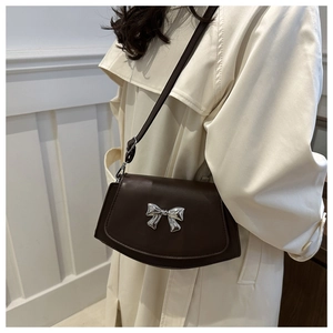 Detail of dark brown fan-shaped shoulder bag with silver bow buckle worn on light coat