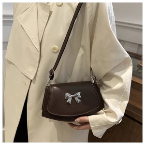 Detail of a dark brown crossbody bag featuring a silver bow accent and leather texture