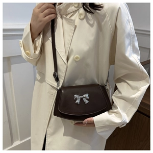 Detail of a dark brown leather crossbody bag with a silver bow accent on a trench coat