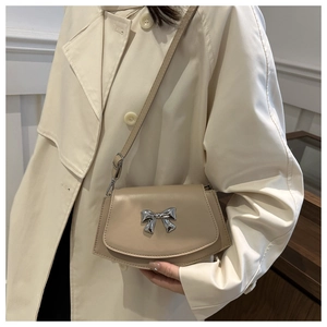 Close-up of a beige saddle bag with a silver bow buckle on a beige trench coat