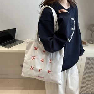 Sac cabas en velours côtelé blanc avec broderie rouge porté à l'épaule dans un style décontracté
