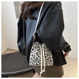 Detail view of leopard print drawstring bucket bag with white leather straps on shoulder