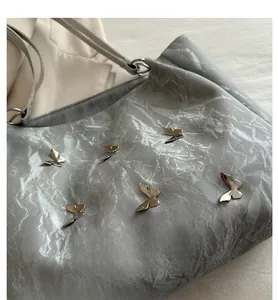 Detail of silver tote bag with metallic butterfly accents and pleated texture