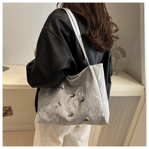 Silver wrinkled tote bag with 3D metallic butterfly details shown on model's shoulder