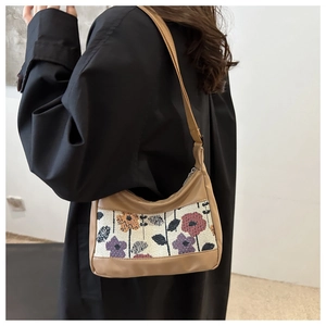 Close-up of vintage floral embroidery and brown PU leather on a crescent shoulder bag