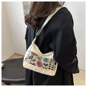 Detailed view of colorful floral embroidery on a white canvas and PU underarm bag