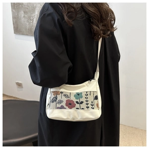 Detail view of white tote bag featuring colorful floral embroidery on a black coat