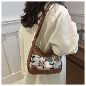 Detail of vintage canvas shoulder bag with floral embroidery and wide strap on a model