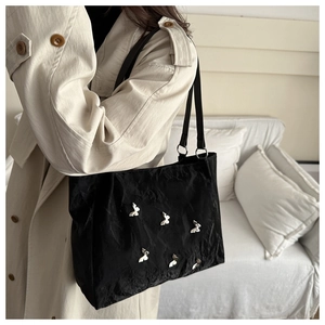 Detail of a black pleated tote bag with silver butterfly charms on a shoulder strap