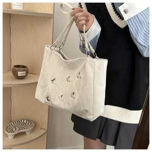 Detail of white textured tote bag featuring six decorative silver metal butterflies
