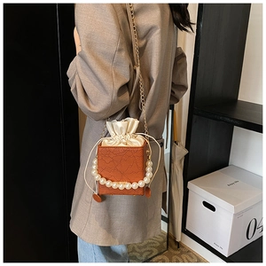 Detail of orange-brown box bag with lace texture, pearl handle, and satin drawstring closure