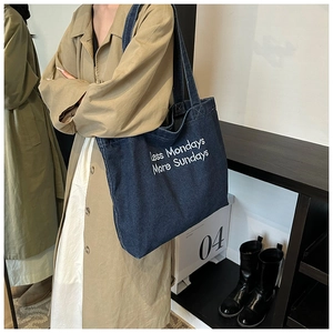 Close-up of deep blue denim tote bag with Less Mondays More Sundays white script embroidery