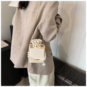 Detailaufnahme der beigen Beuteltasche mit Perlengriff und goldenem Kettenriemen