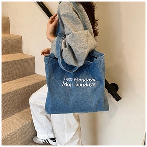 Detail of blue denim tote bag with Less Mondays More Sundays embroidery and wide strap