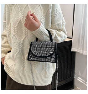 Detail shot of a black rhinestone crossbody bag with silver chain on white sweater