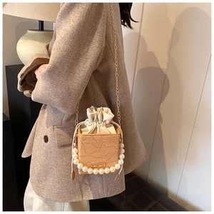 Detail of lace crossbody box bag with pearl handle and golden chain on a model