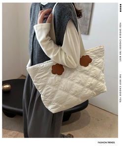 Detail of white quilted tote bag featuring brown flower-shaped leather patches on straps