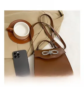 Close-up of brown leather bag with silver bow rhinestone buckle and top handle detail