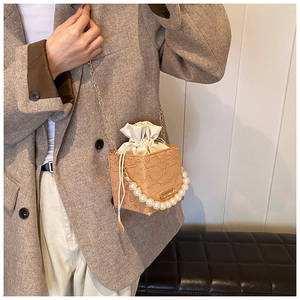 Detail of light brown lace bucket bag featuring pearl handle and gold chain strap