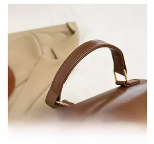 Close-up of brown PU leather handbag handle with fine stitching and gold metal buckles