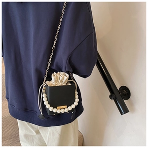 Detail einer schwarzen Eimer-Tasche mit Perlengriff und goldener Ketten-Schultergurt