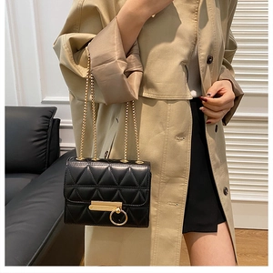 Classic black quilted crossbody bag with gold hardware worn on a beige trench coat