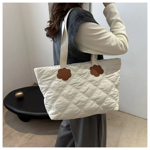 Detail view of large white quilted tote bag with floral leather accents on a female model