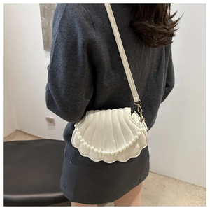 Detail of shell-shaped crossbody bag with pearl chain and beige quilted texture on model