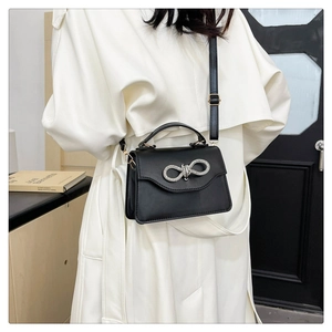 Close-up of black square bag with diamond bow buckle on model's white coat
