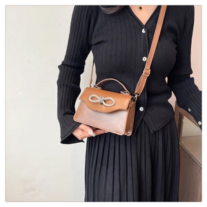 Detail of brown leather handbag featuring a sparkling rhinestone bow buckle and strap