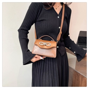 Detail of a brown crossbody bag with bow buckle decoration on a black dress