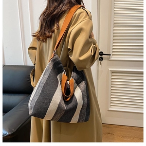 Model wearing a large striped canvas tote bag with contrast orange straps in casual setting
