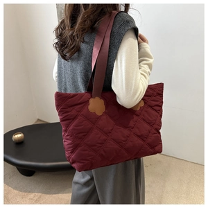 Macro detail of wine red quilted tote bag featuring a leather floral shoulder strap patch