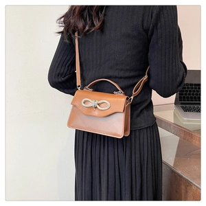 Brown crossbody square bag with a sparkling rhinestone bow buckle shown on a model