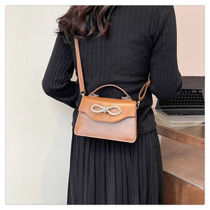 Brown crossbody bag with rhinestone bow detail shown on a model in a lifestyle setting