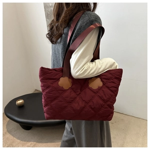 Detail of burgundy quilted tote bag featuring stylish brown floral leather patch accents