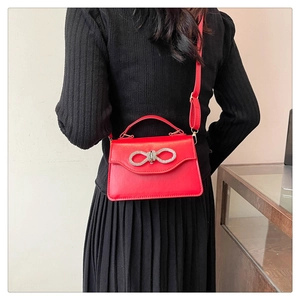 Detail of red leather crossbody bag with sparkling rhinestone bow on black dress