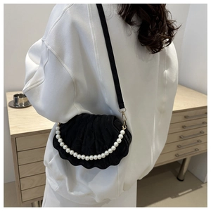 Detail view of black shell-shaped crossbody bag with pearl handle and wavy edge design