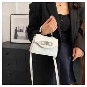 Close-up of a white leather crossbody bag featuring a sparkling rhinestone bow buckle