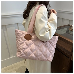 Detail of pink quilted tote bag featuring a brown petal-shaped leather patch and wide strap
