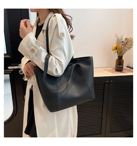 Detail of a large black matte leather tote bag featuring a Fashion label on a model