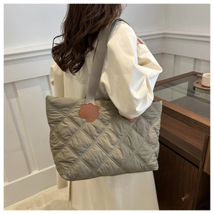 Close-up of quilted grey-green tote bag featuring a unique orange petal-shaped leather patch