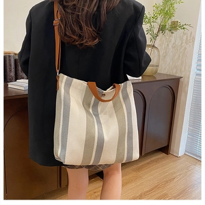 Vertical grey and white striped canvas tote bag with brown straps in a cozy home setting